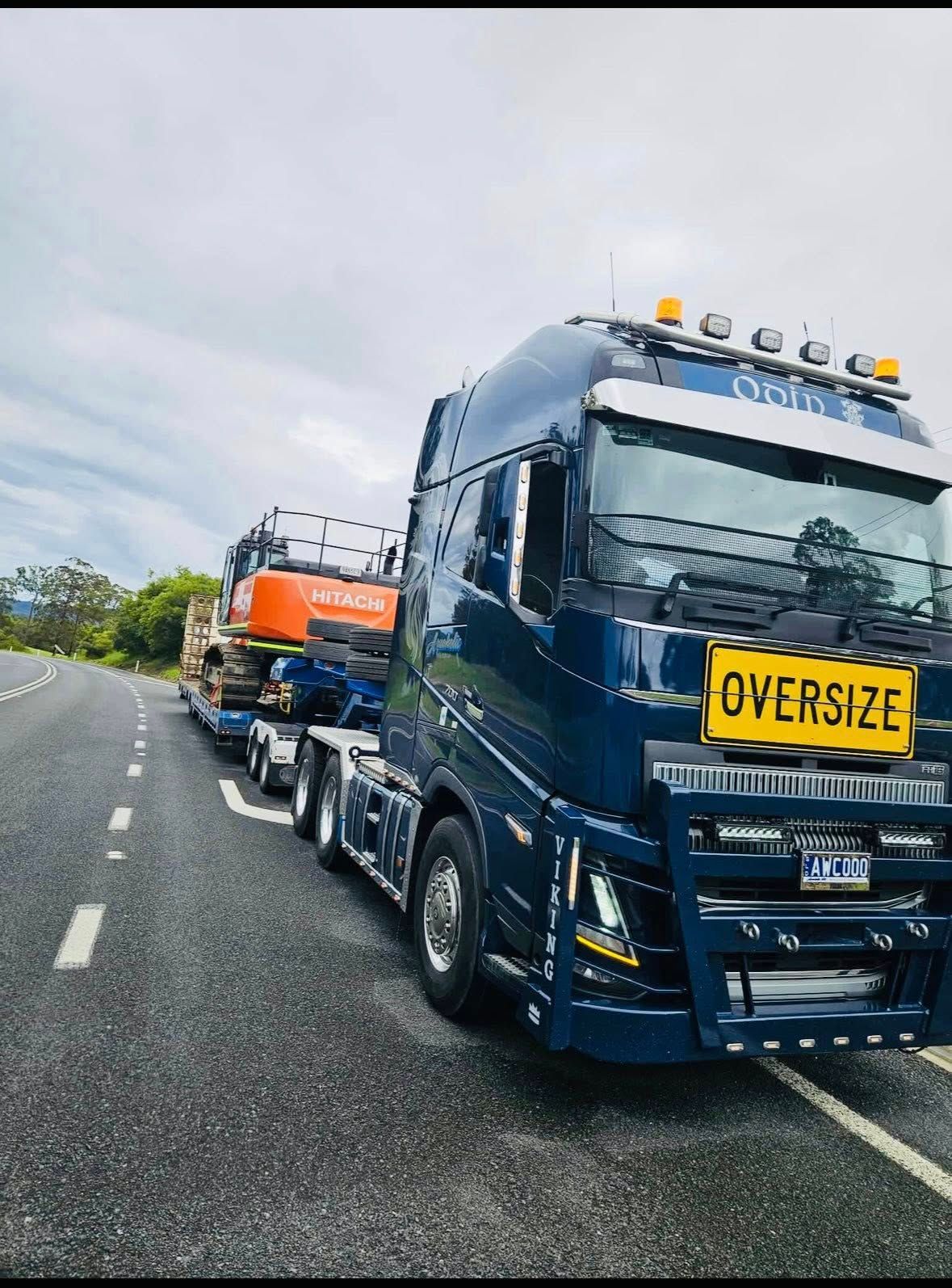 A Dark Blue Semi-truck With a Sign Hauling an Orange Excavator — Mid North Coast Heavy Vehicle Repairs In Thrumster, NSW