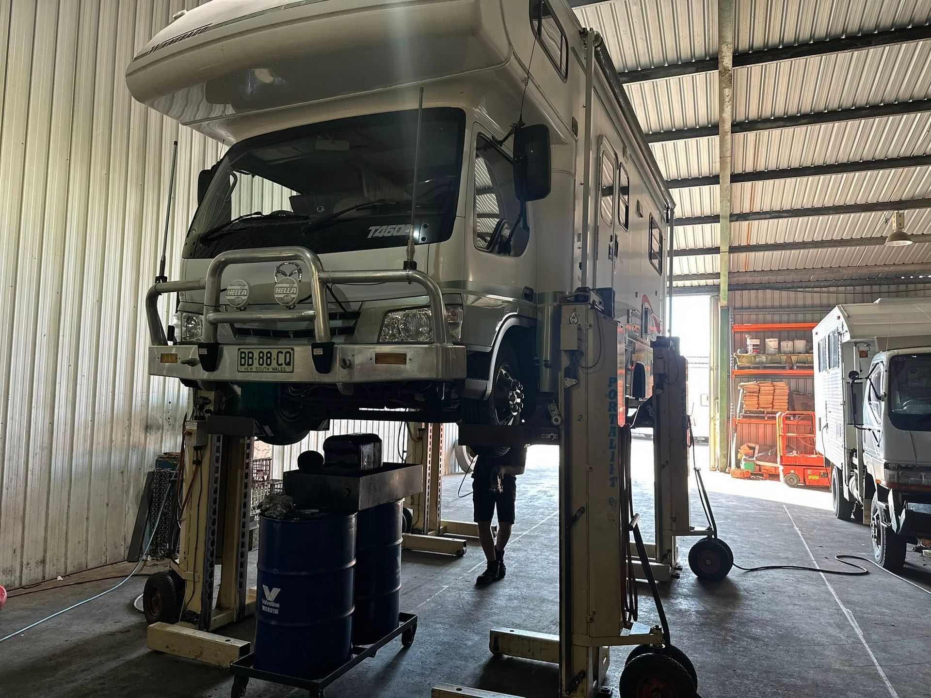 A White Motorhome Raised on a Hydraulic Lift in a Garage — Mid North Coast Heavy Vehicle Repairs In Wauchope, NSW