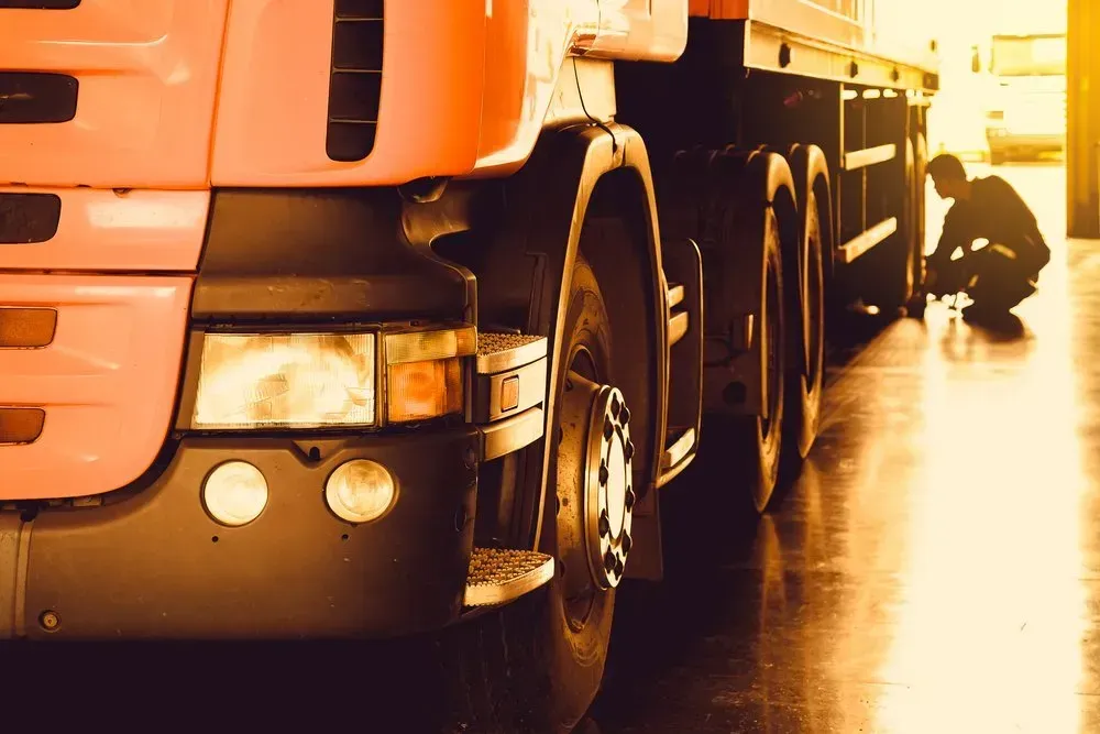 A Mechanic Kneeling to Inspect the Wheels of a Semi-truck — Mid North Coast Heavy Vehicle Repairs In Wauchope, NSW
