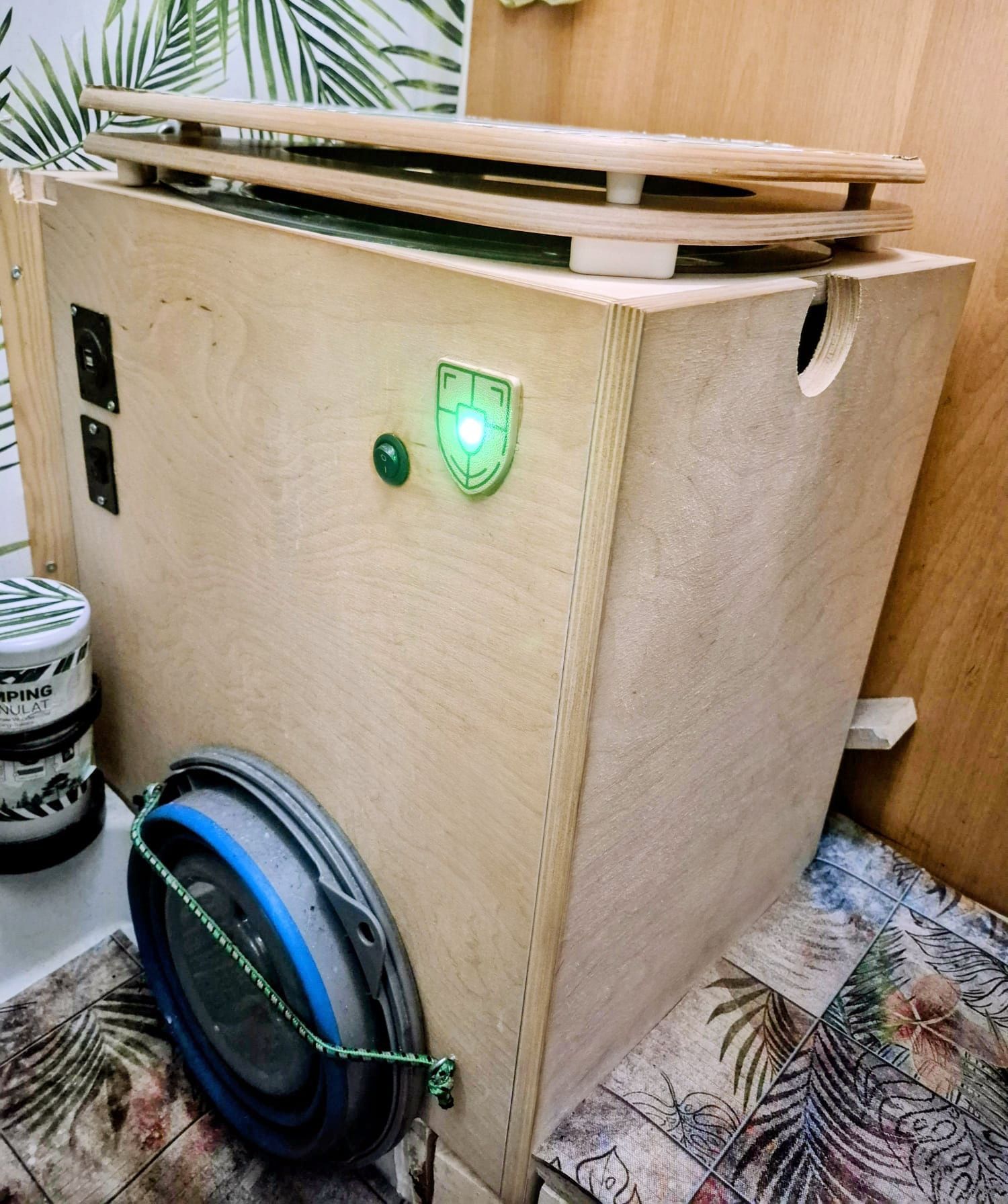 Holzkiste mit grüner Kontrollleuchte, Eimer und Stauraum, wahrscheinlich für einen Camper oder einen kleinen Raum.