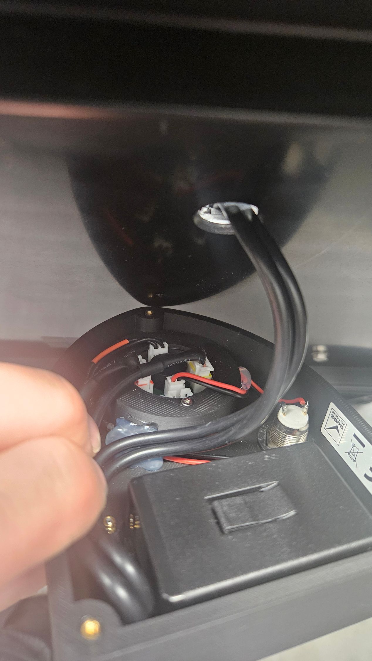Eine Hand greift in eine offene schwarze Box, die Drähte und elektronische Bauteile enthält; ein Kabel ragt aus der Box heraus.