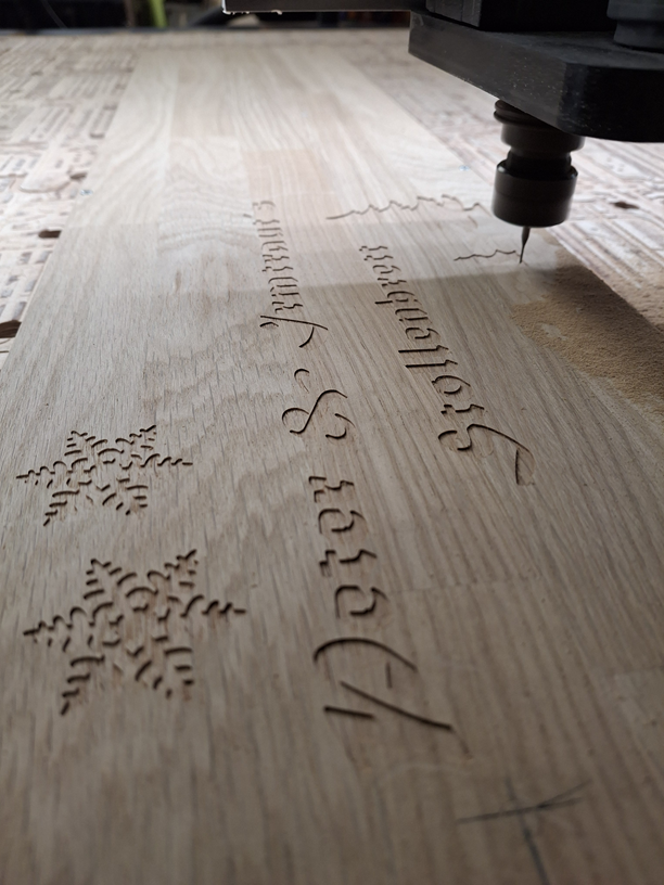 Eine CNC-Maschine graviert Text und Schneeflocken in ein Holzbrett.