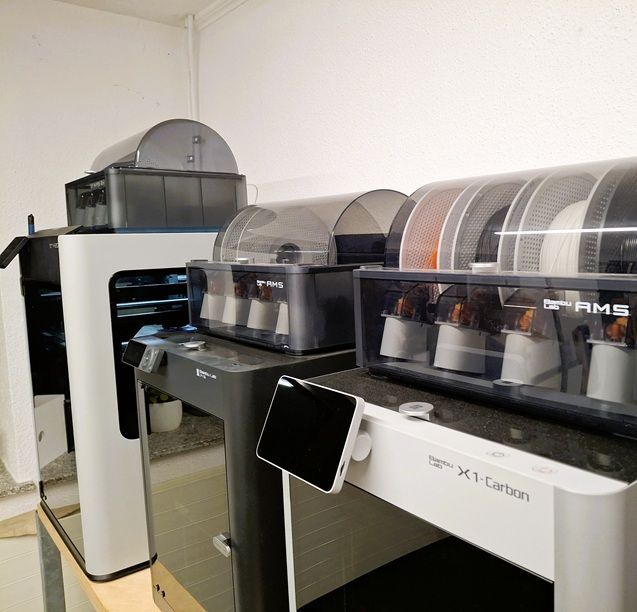 Mehrere 3D-Drucker, jeder mit Filament bestückt, in einem hell erleuchteten Raum.