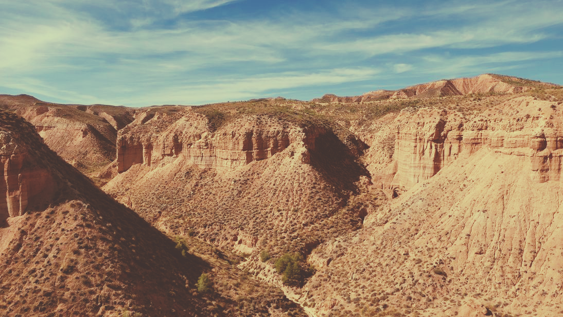 Canyonlandschaft mit rötlich-braunen Felsformationen unter einem teilweise bewölkten blauen Himmel.