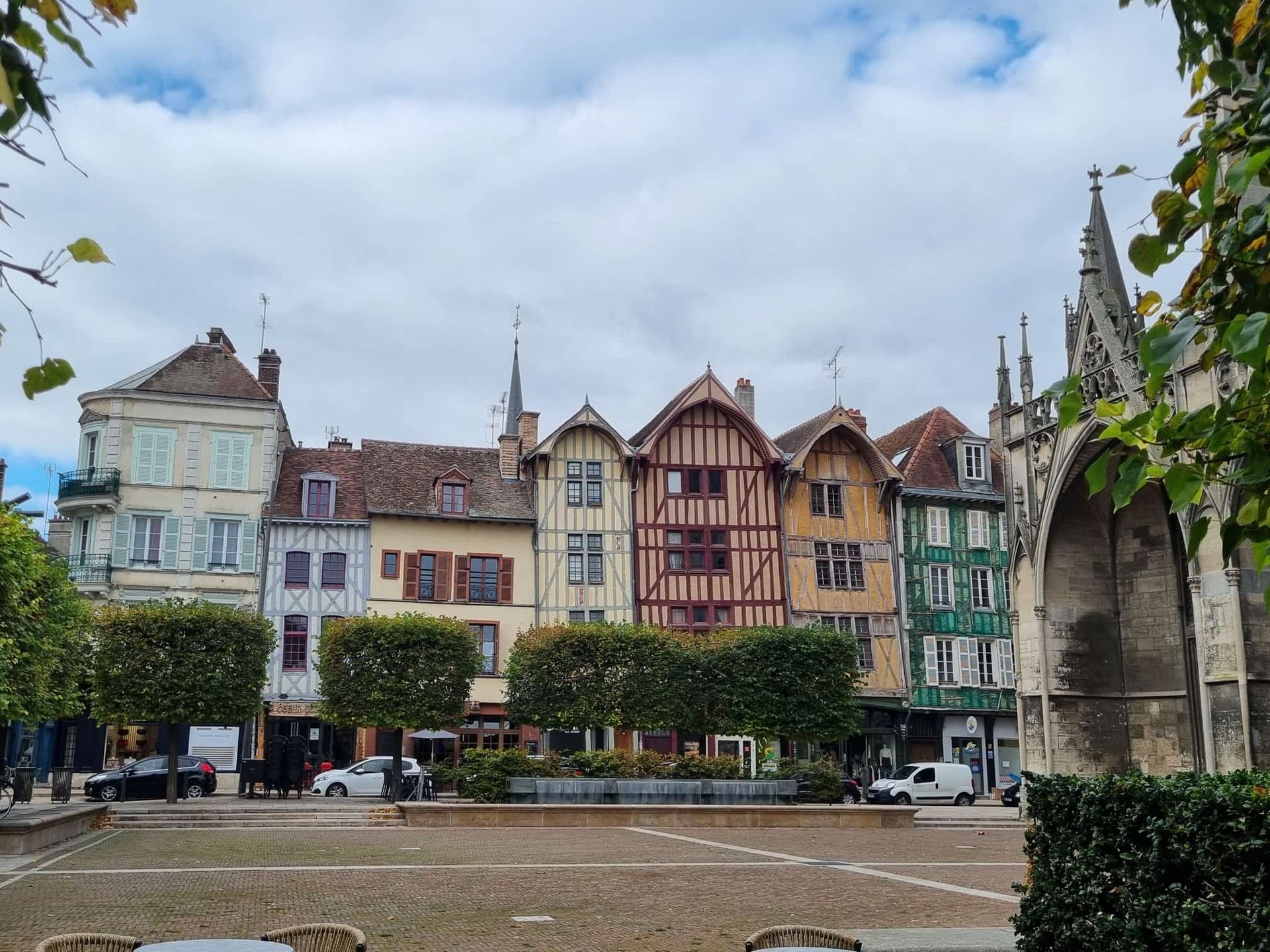 Bunte Fachwerkhäuser säumen einen Platz in einer europäischen Stadt; rechts ist eine Kirche zu sehen.
