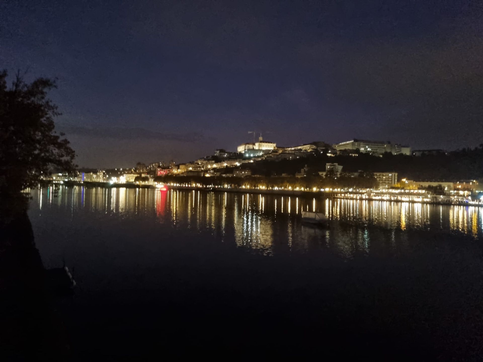 Nachtansicht eines Flusses, in dem sich die Lichter der Stadt und die Gebäude an einem fernen Hügelhang spiegeln.