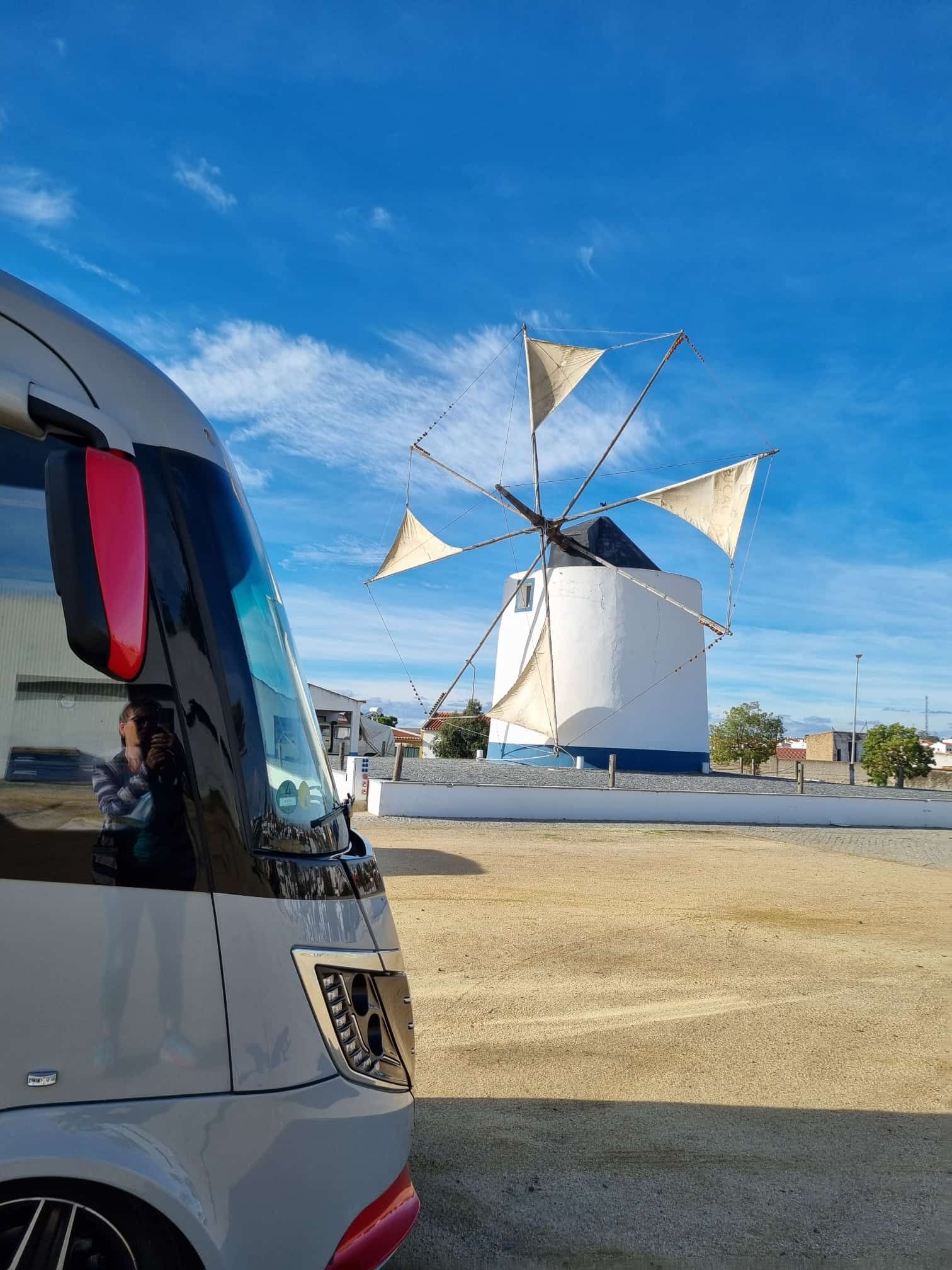 Ein grau-roter Wohnwagen parkt an einem sonnigen Tag in der Nähe einer weißen Windmühle.
