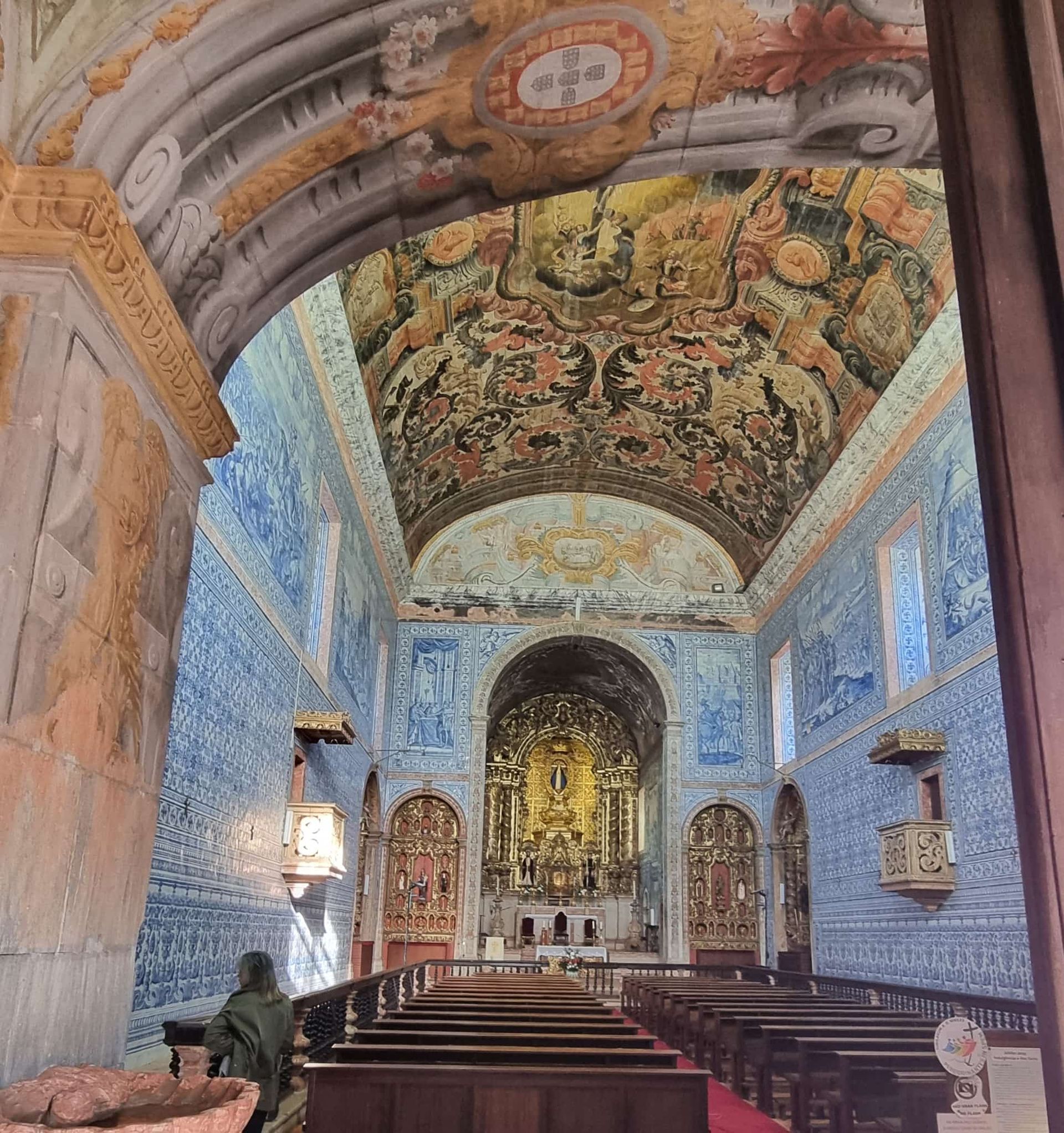 Innenansicht einer Kirche mit blau-weiß gefliesten Wänden, einer bemalten Decke und einem goldenen Altar.