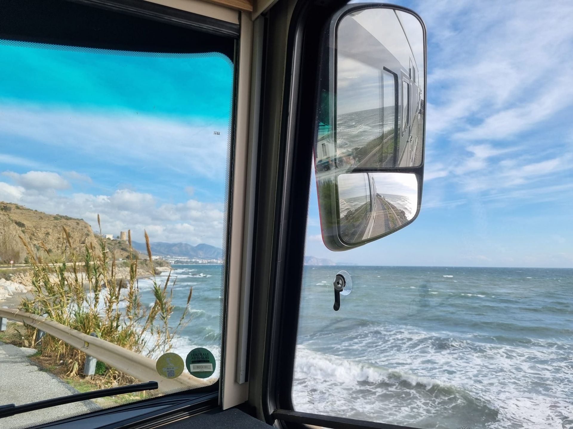 Blick aus dem Fahrzeugfenster auf den Ozean, die Küstenlinie und den Seitenspiegel, der die Straße reflektiert.