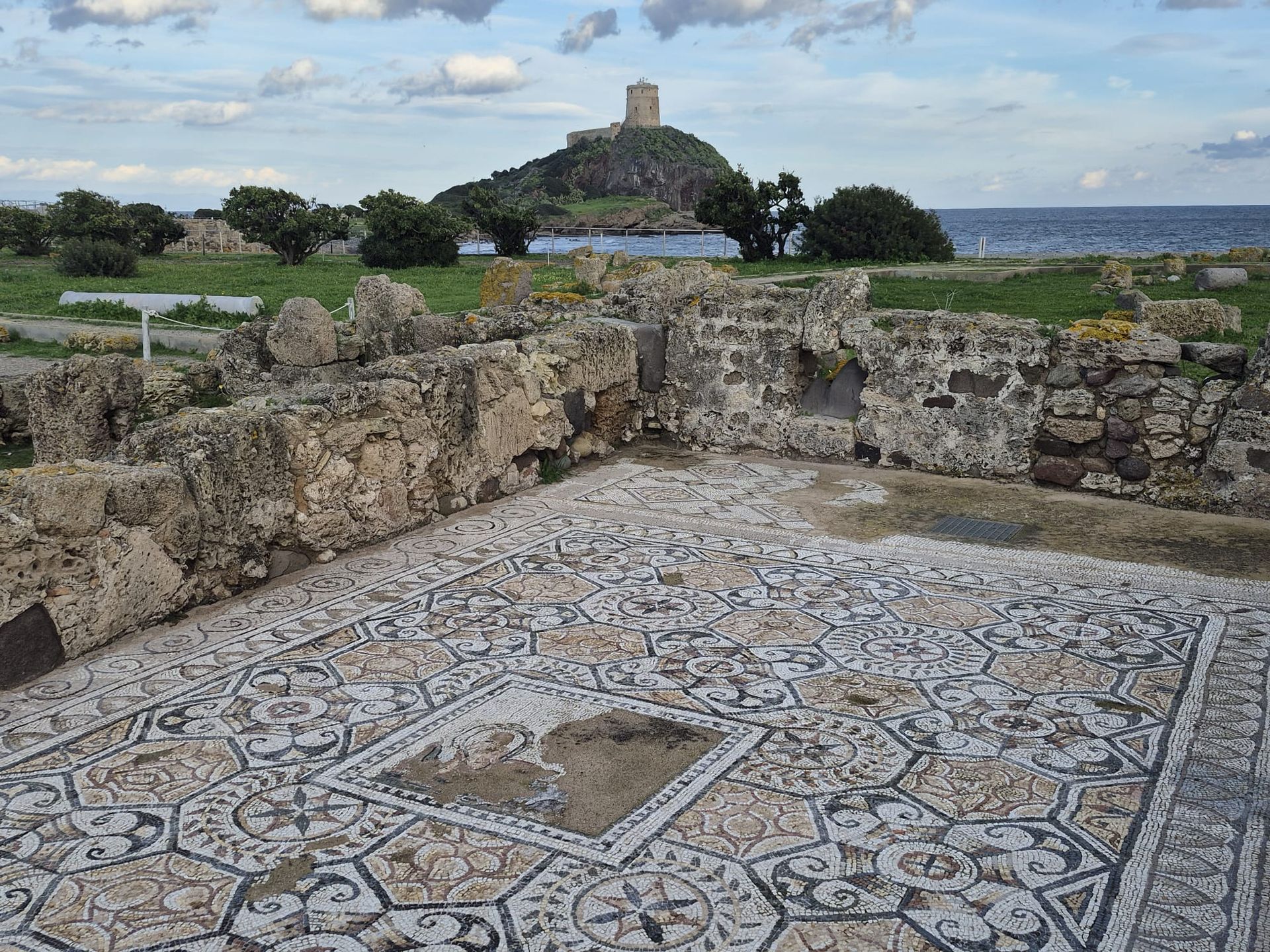 Antiker Mosaikboden mit Ruinen, Meer und Turm auf einem Hügel.