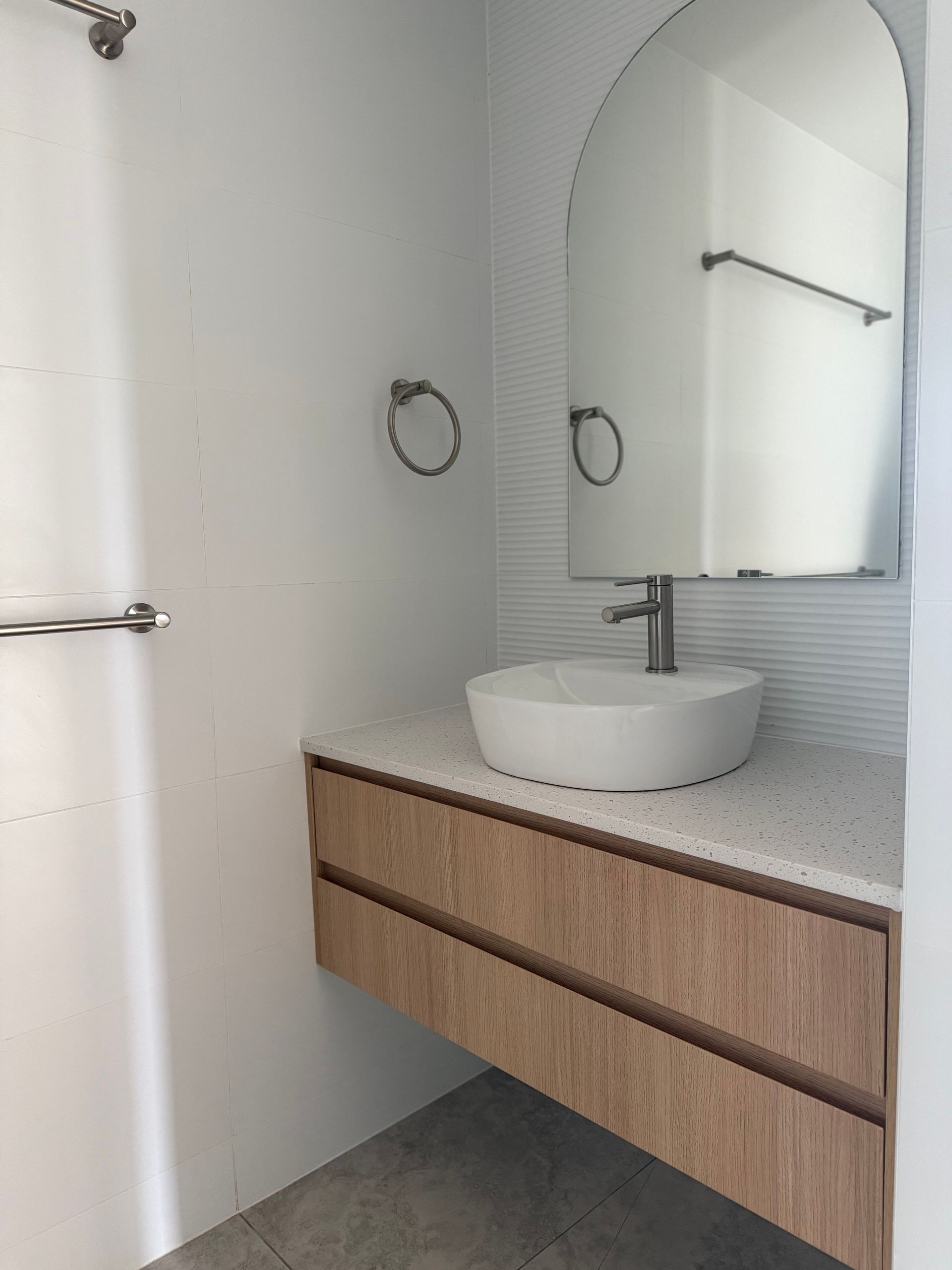 Modern bathroom with floating wooden vanity, white vessel sink, arched mirror, and chrome fixtures — Canelo Cabinetry In Rocklea, QLD