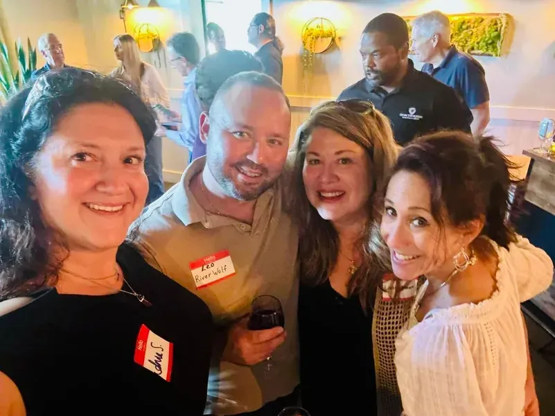 Four people smiling and posing together at an indoor social event with drinks.