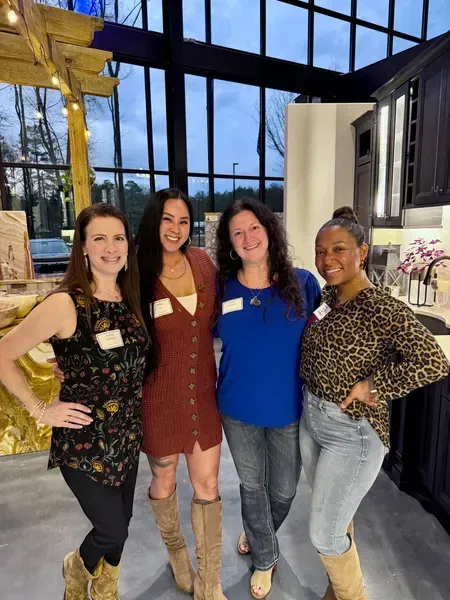 Four people posing indoors, smiling in front of tall windows and a decorative display.