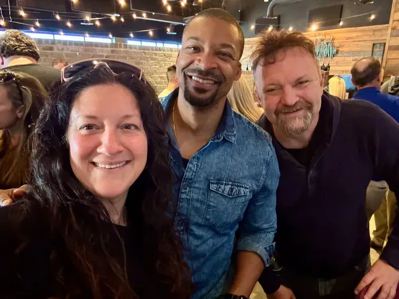 Three smiling people posing together in a warmly lit indoor venue