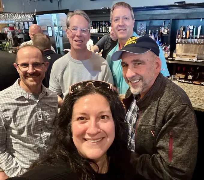 Five smiling people posing together in a bar or restaurant.