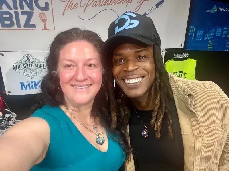 Two people smiling for a selfie at an indoor event, with posters in the background.