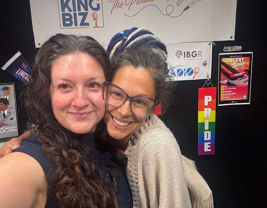 Two smiling people posing at a booth with colorful “PRIDE” signage in the background
