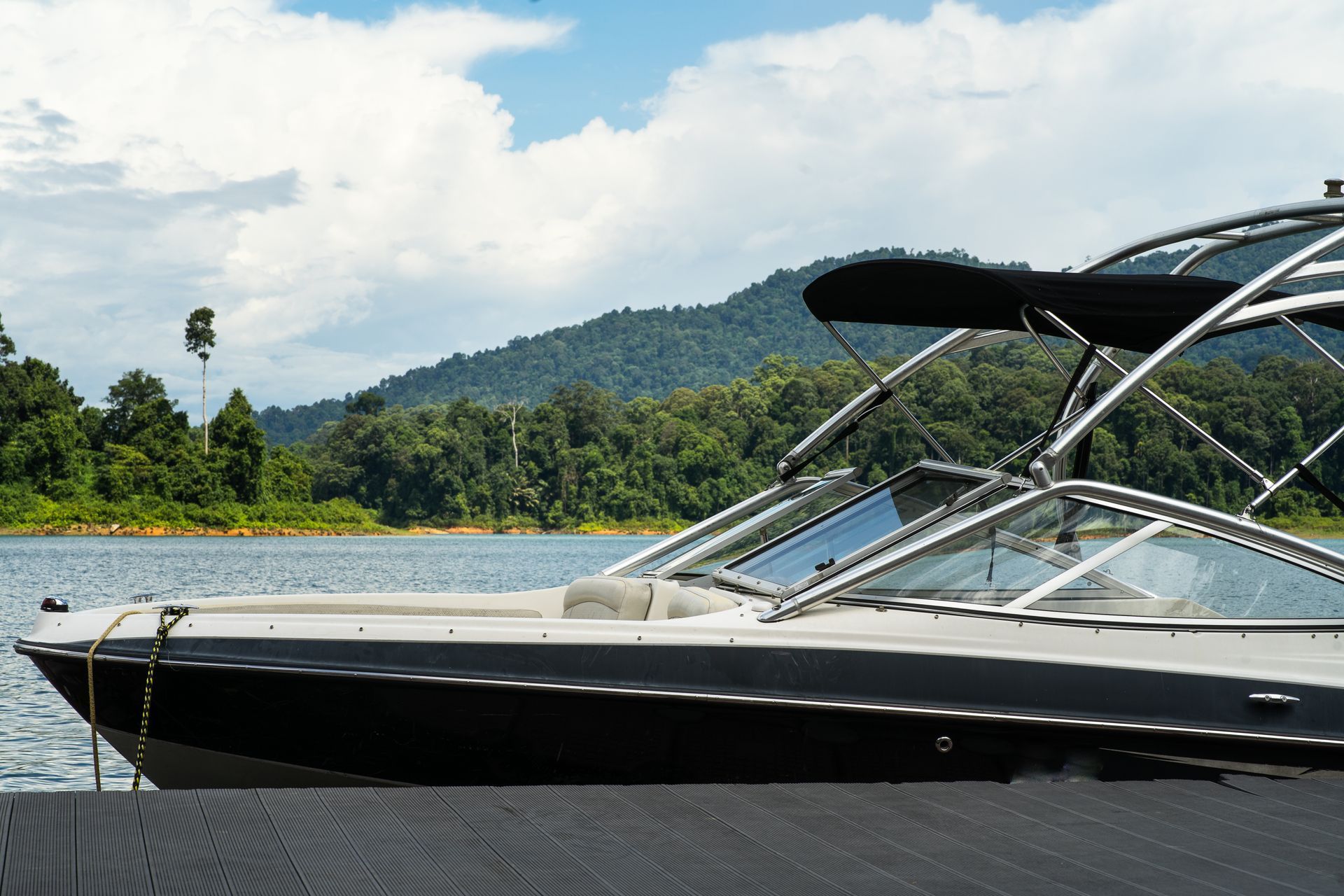 Boat docked on a lake, with a backdrop of mountains and trees under a cloudy sky.