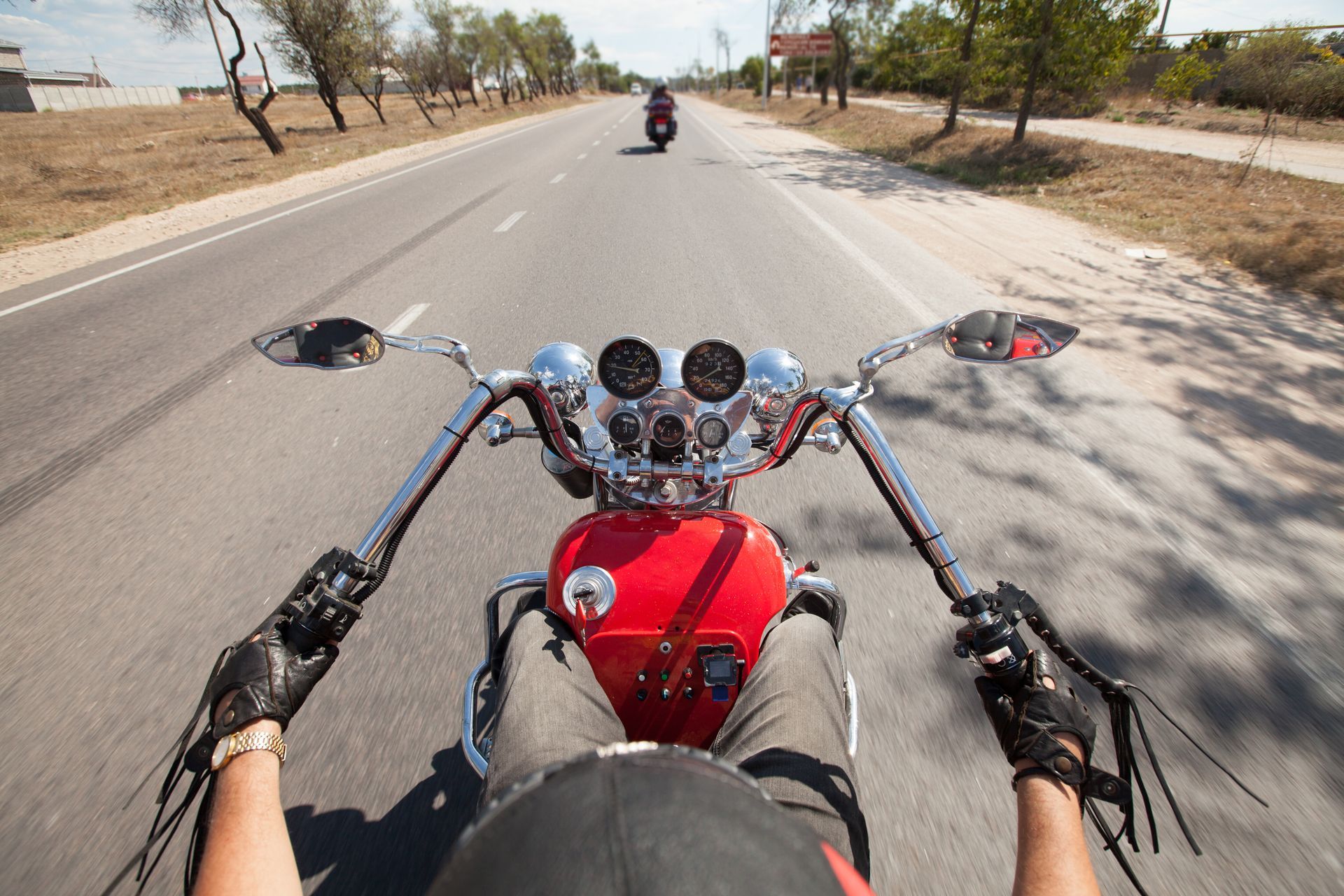 Motorcycle rider's view on a road, following another motorcycle. Red bike with chrome details, sunny day.