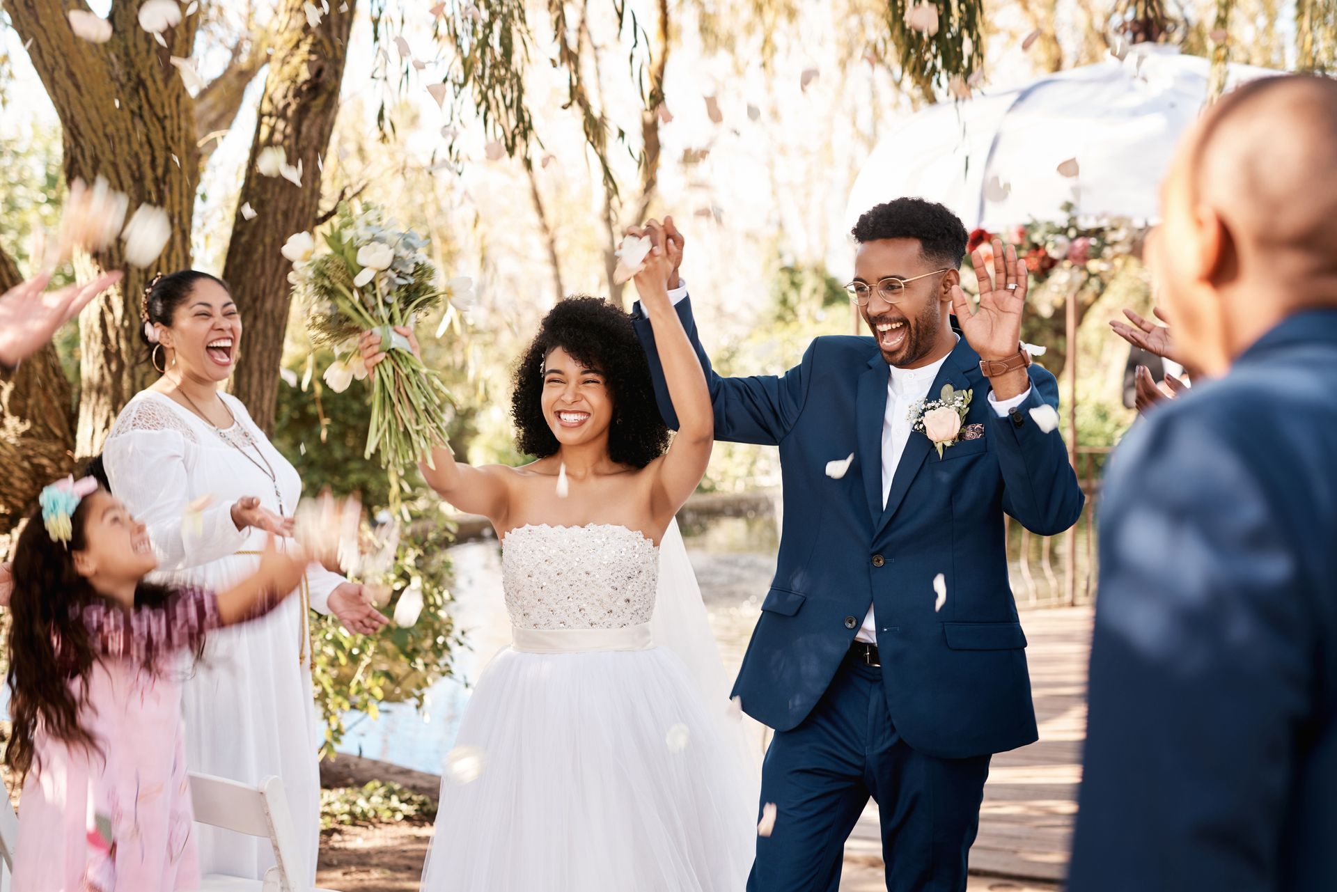 Newly married couple celebrates amidst falling petals, cheered by guests.