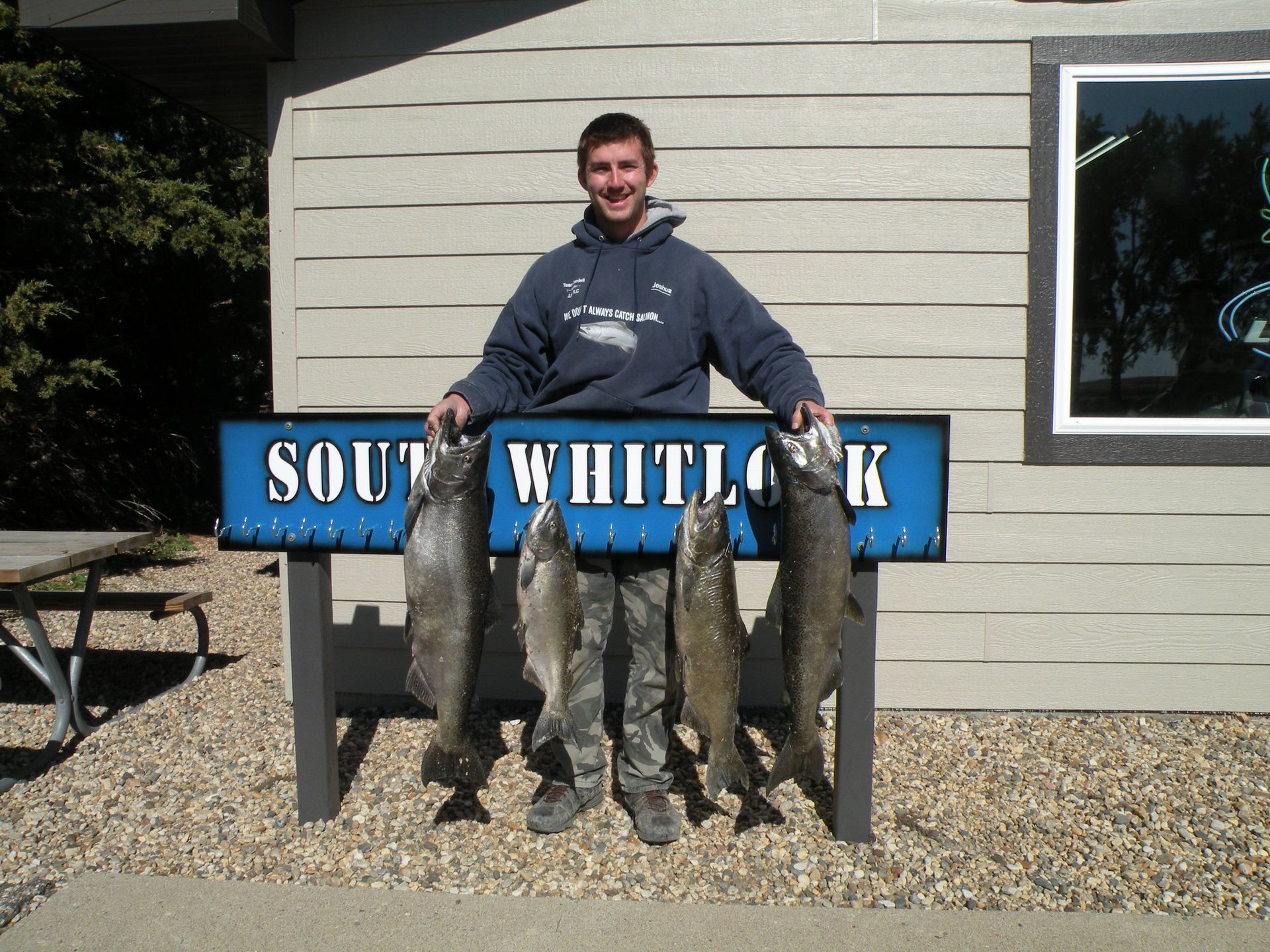 A man holding four fish in front of a sign that says south whitlock