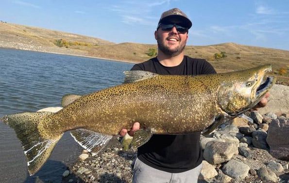 A man is holding a large fish in front of a lake.