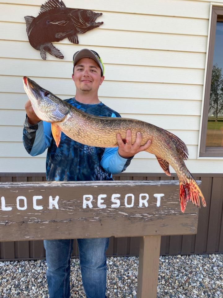 A man is holding a large fish in front of a sign that says lock resort.