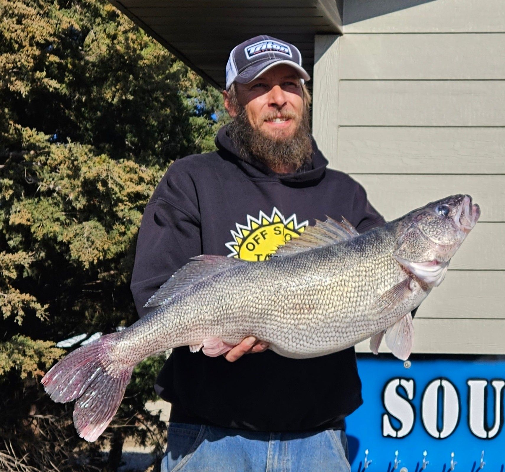 A man holding a large fish in front of a sign that says sou