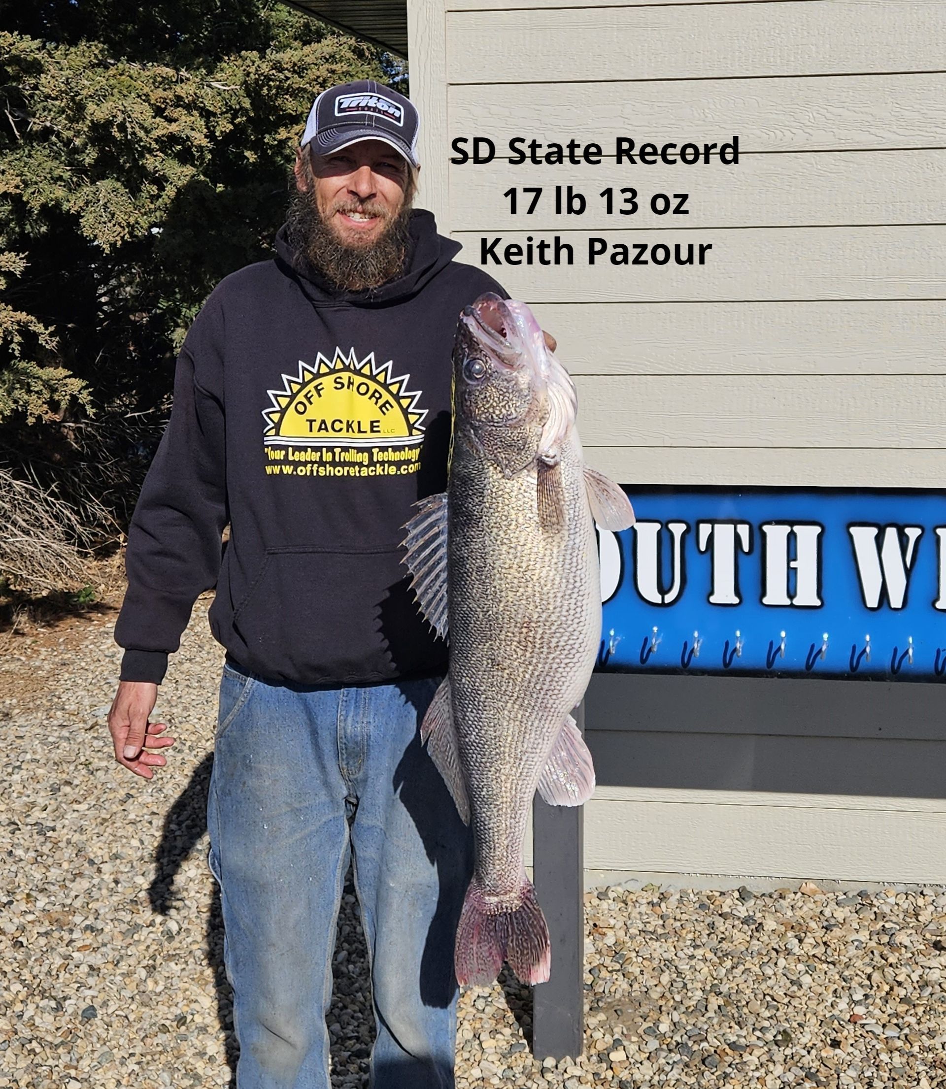 A man holding a large fish in front of a sign that says sd state record