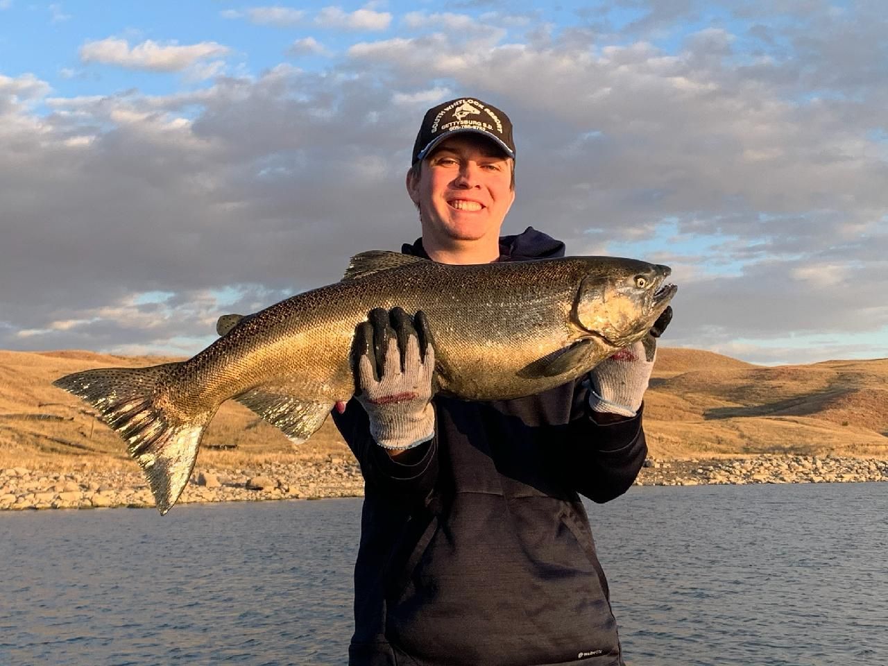 A man is holding a large fish in his hands in front of a lake.