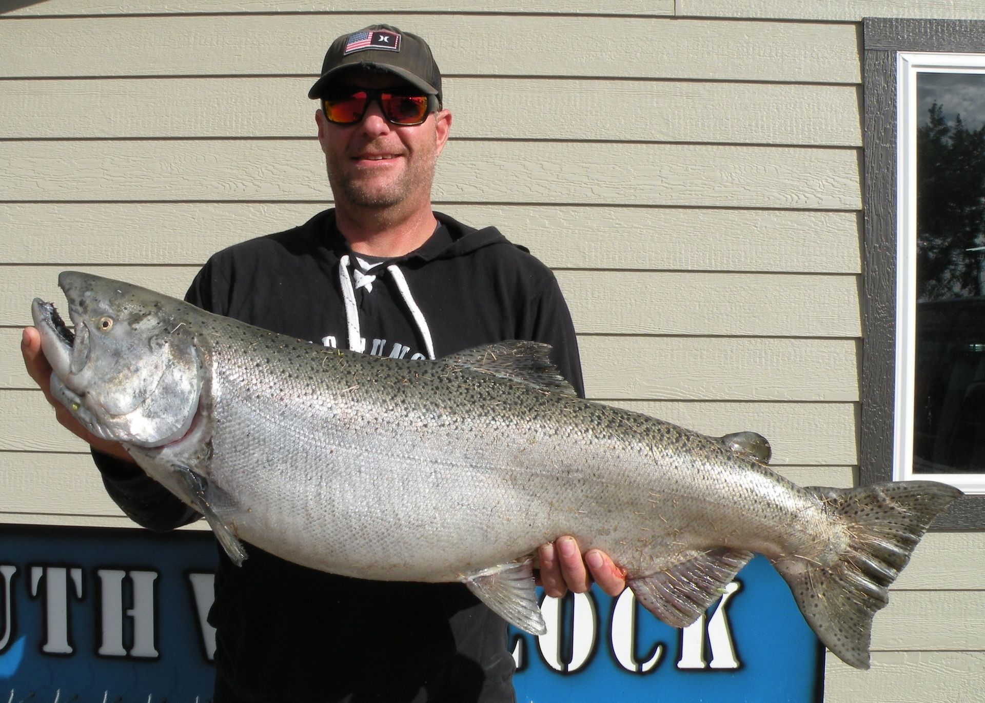 A man is holding a large fish in front of a sign that says south dock