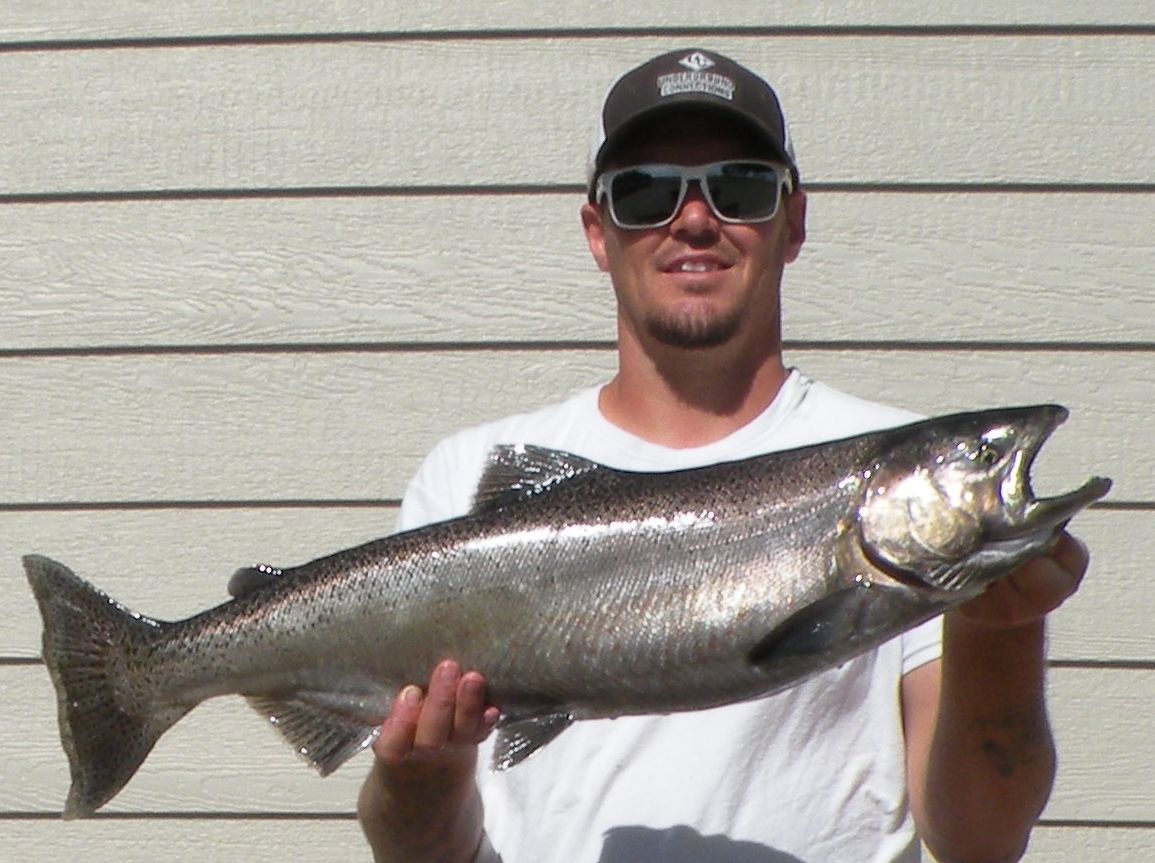 A man wearing sunglasses and a hat is holding a large fish