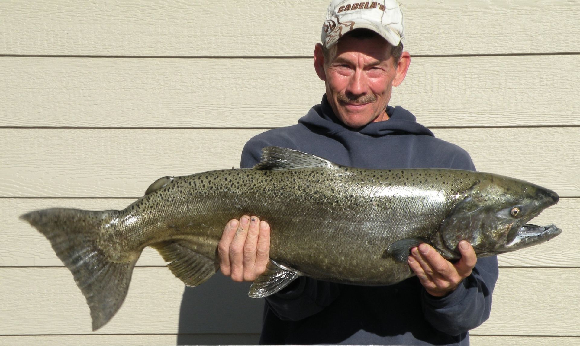 A man in a columbia hat is holding a large fish