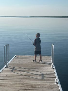 A young boy is fishing on a dock in the water.