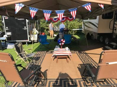 A group of people are sitting under a tent with american flags hanging from it.