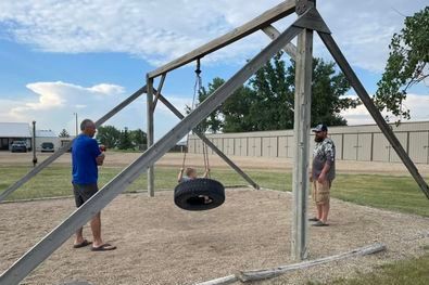Two men are standing next to a tire swing in a park.
