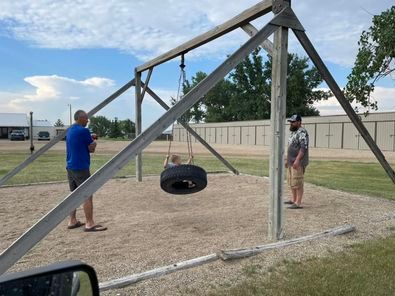 Two men are standing next to a tire swing in a park.