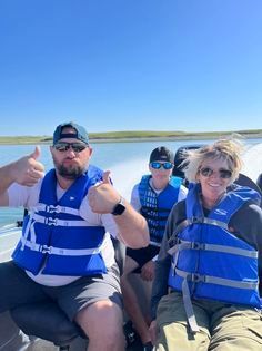 A group of people wearing life jackets are sitting on a boat giving a thumbs up.