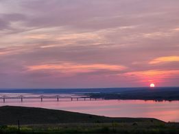 A sunset over a body of water with a bridge in the distance.
