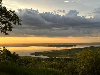 A sunset over a large body of water with trees in the foreground.