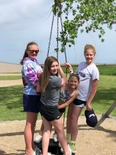 A group of young girls are standing next to each other on a swing.