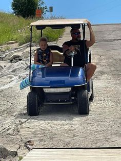 A man and a child are riding a golf cart down a dirt road.