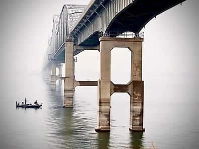 A boat is floating under a bridge in the water.