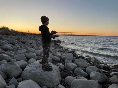 A young boy is fishing on the shore of a lake.
