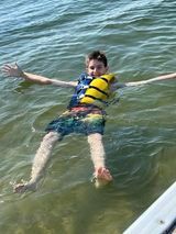 A young boy is floating on his back in the water wearing a life jacket.