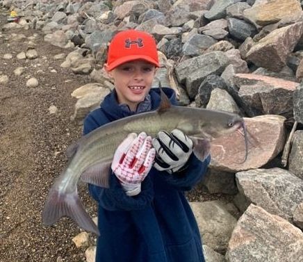 A young boy is holding a catfish in his hands.
