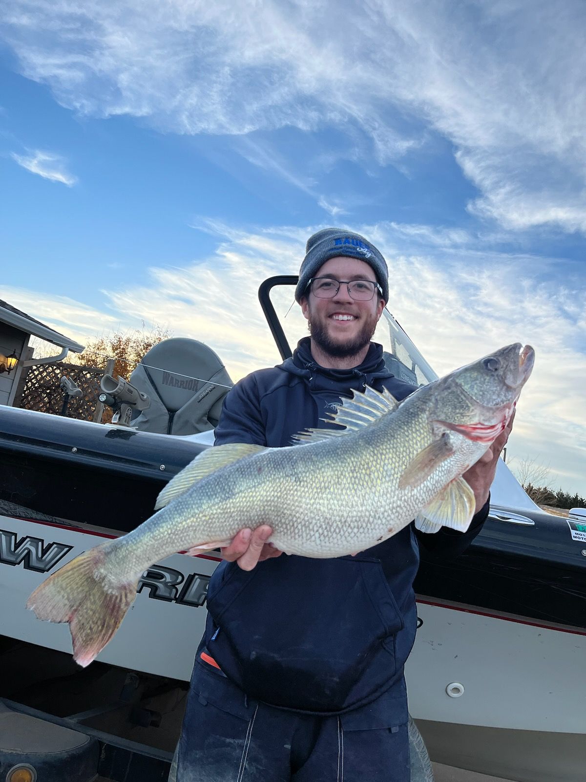 A man is holding a large fish in front of a boat.