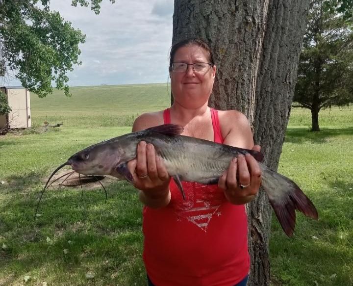 A woman in a red tank top is holding a catfish in her hands.