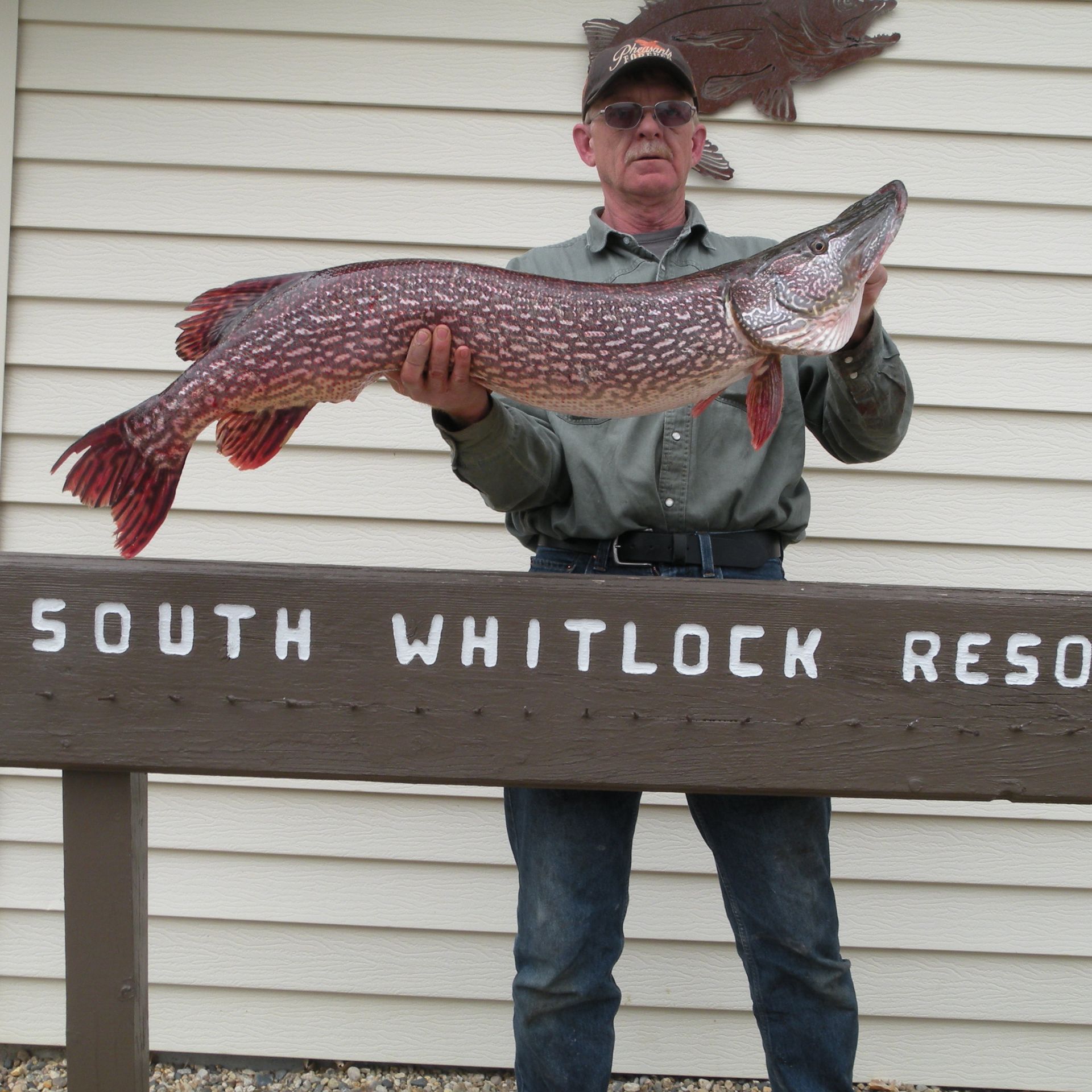 A man holding a large fish in front of a sign that says south whitlock resort