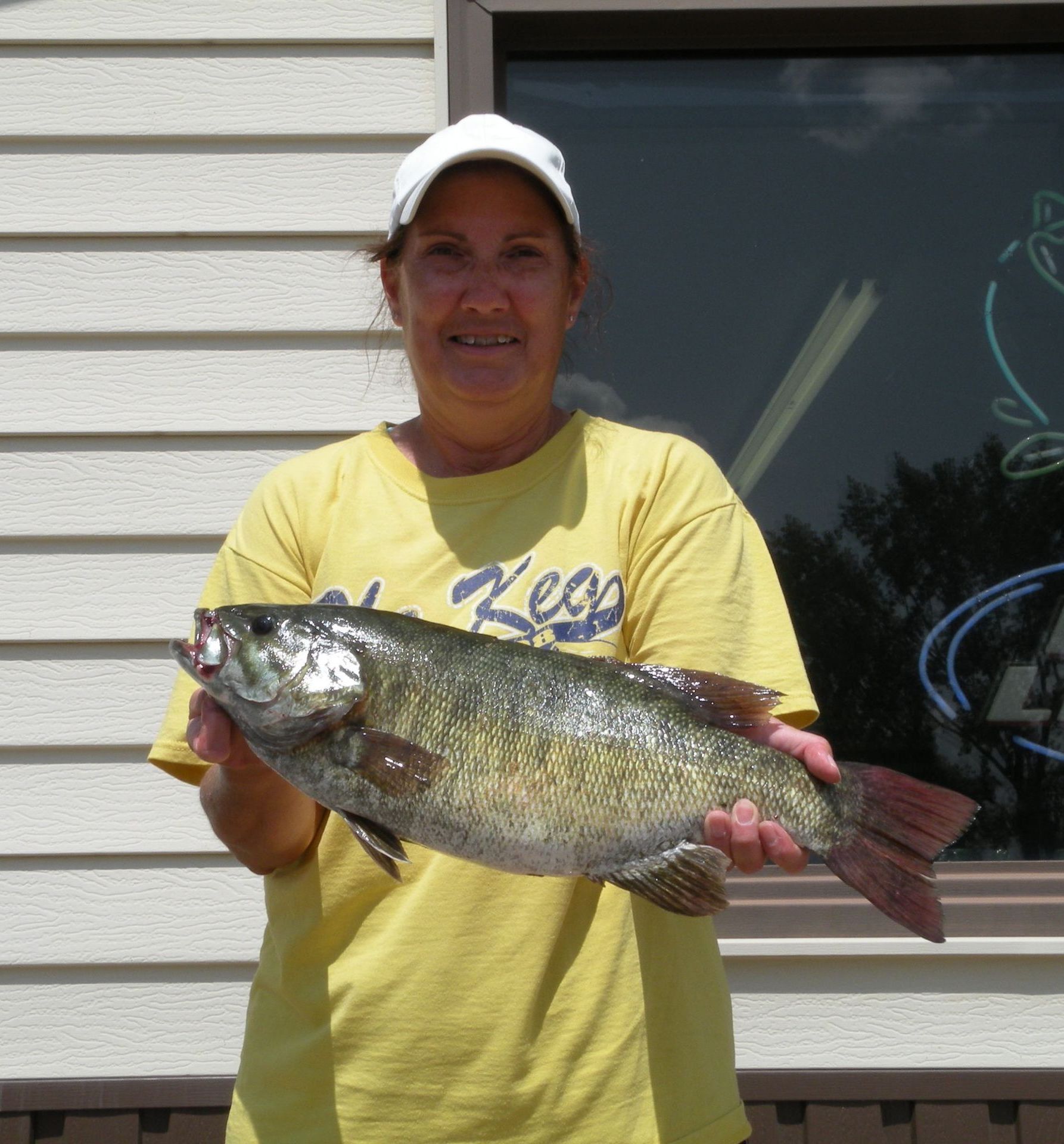 A woman in a yellow shirt holding a large fish